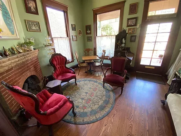Sage green room with red brick fireplace, velvet chairs, and patterned rug.