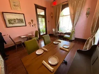 Brightly lit dining room with pink walls, wood table, and lime green chairs.
