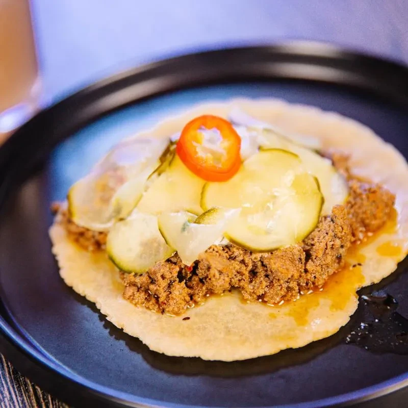 Open-faced taco with ground meat, melted cheese, pickles, and chili.
