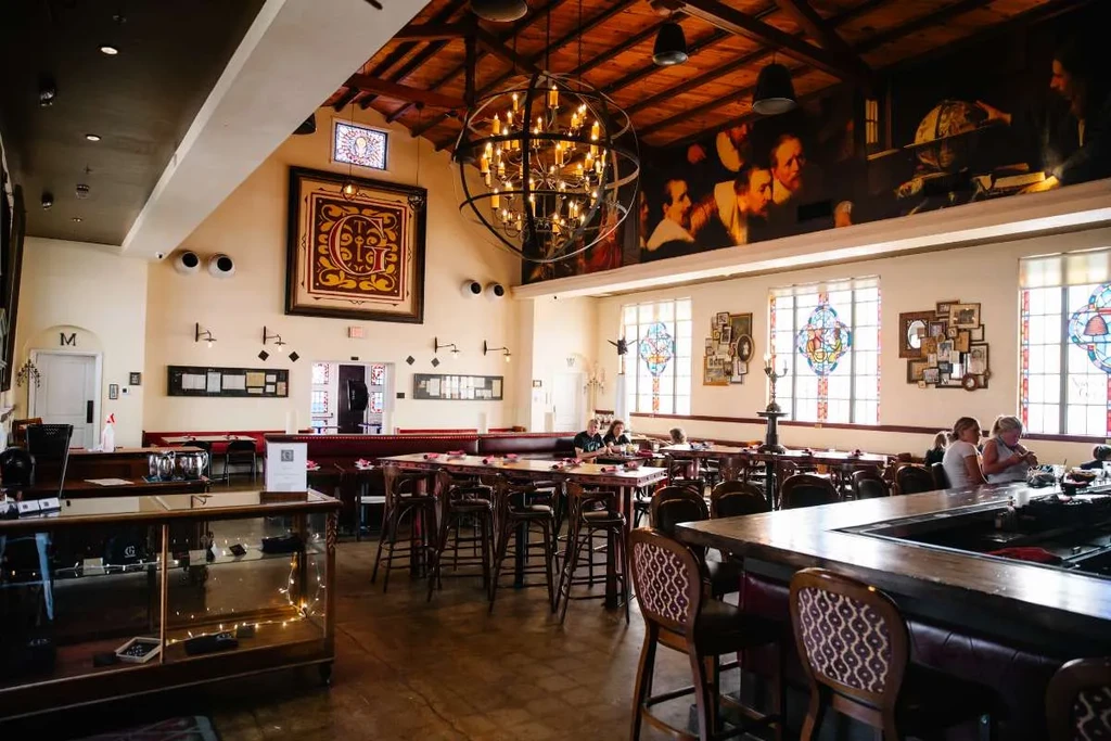 Elegant restaurant interior with exposed beams, large chandelier, and patrons.