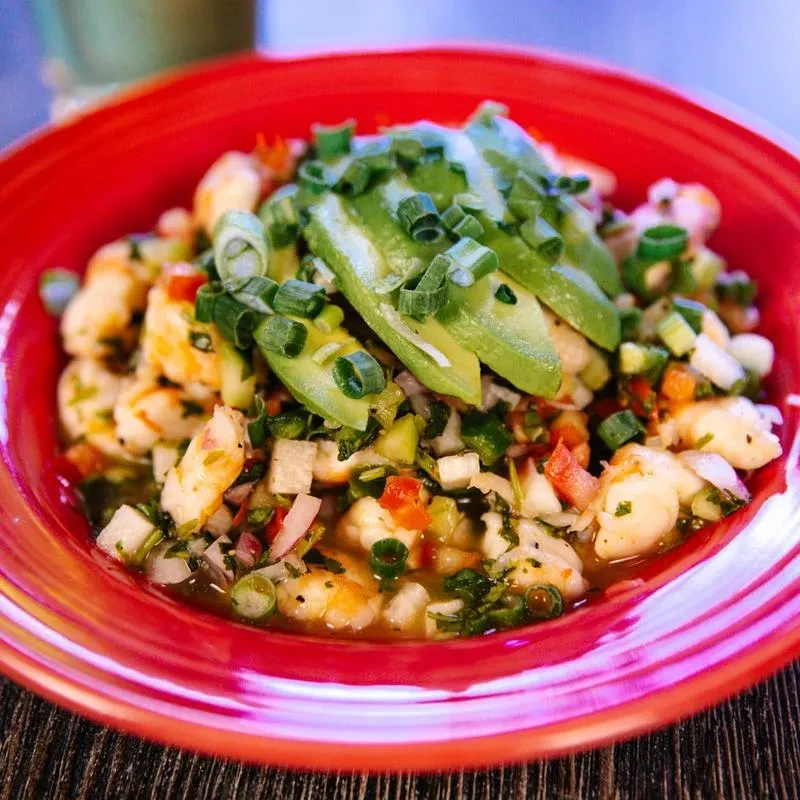 Close-up of shrimp ceviche with avocado and vegetables in a red bowl.