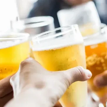 Hands clinking cold pint glasses of frothy golden beer in a toast.