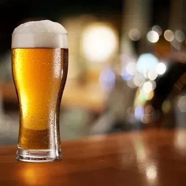 Cold golden beer with frothy head on a wooden surface.