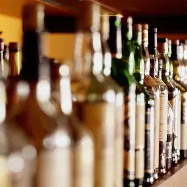 Blurred row of various liquor bottles on a dim bar shelf.