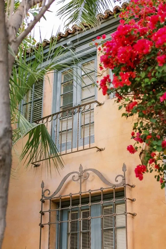 Mediterranean stucco building with blue shutters, ironwork, and red bougainvillea.