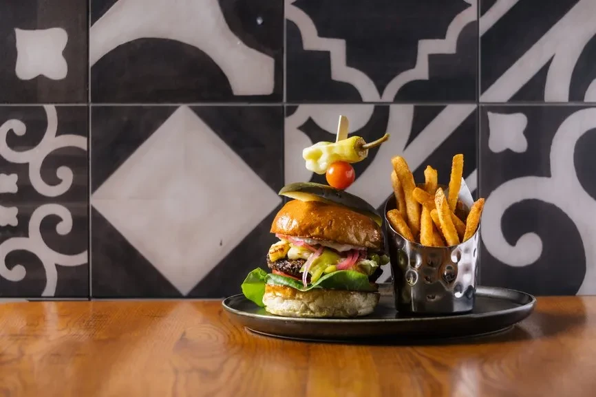 Burger, fries, and skewer on a dark plate, tiled background.
