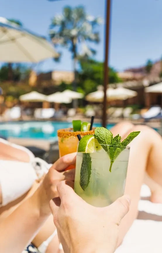 Close-up of two cocktails held by people poolside at a resort.