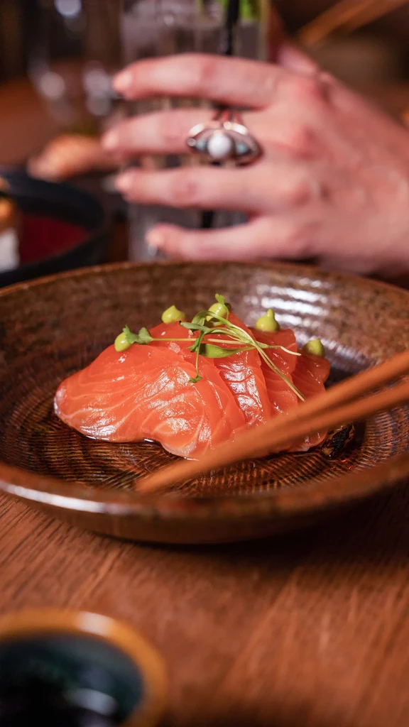 Salmon sashimi with green sauce, microgreens, and chopsticks in a ceramic bowl.
