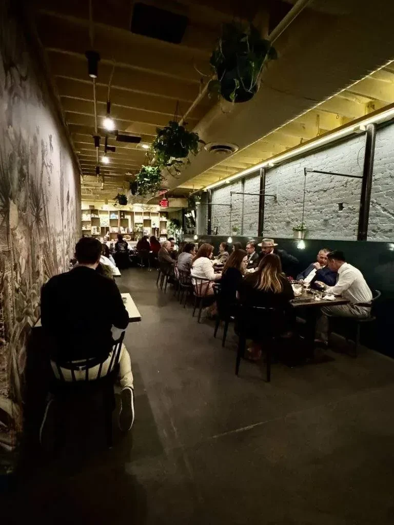 Dimly lit restaurant with botanical mural, exposed beams, and seated patrons.