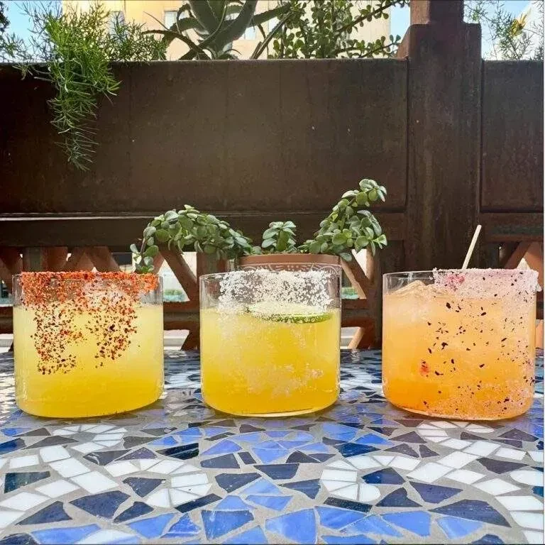 Three vibrant cocktails with spiced rims on a tiled outdoor table.
