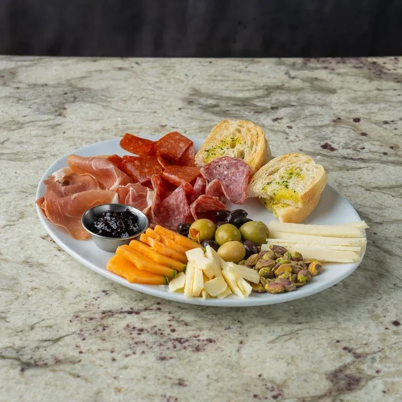 Charcuterie board with cured meats, cheeses, olives, pistachios, bread, jam.