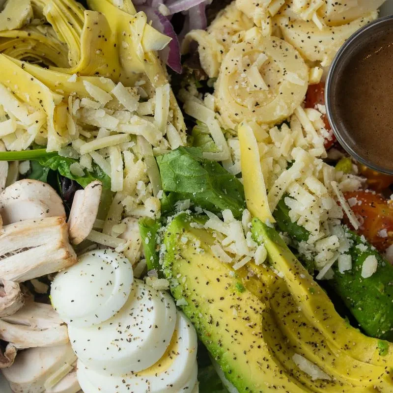 Top-down colorful salad featuring avocado, egg, cheese, artichokes, and greens.