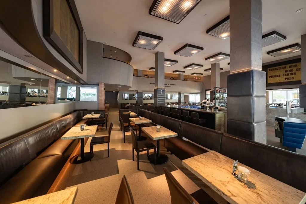Spacious modern restaurant interior with booths, bar, concrete columns, and signs.
