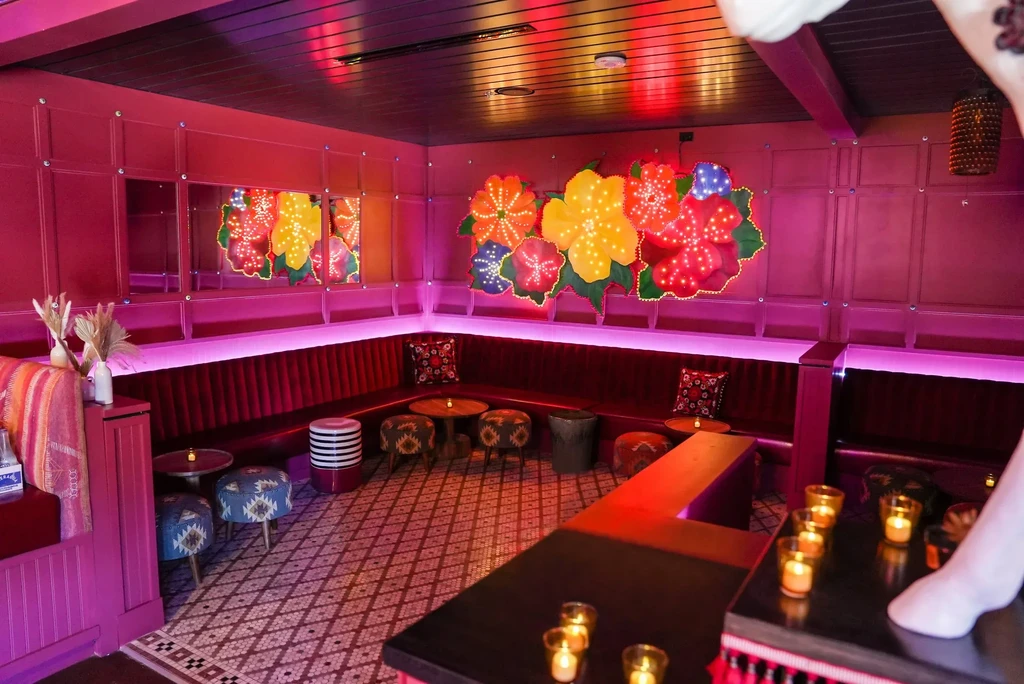 Eclectic bar interior with magenta walls, floral art, and mannequin leg.
