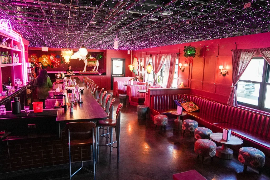 Bar interior: pink lights, red booths, wooden bar, and white animal statue.