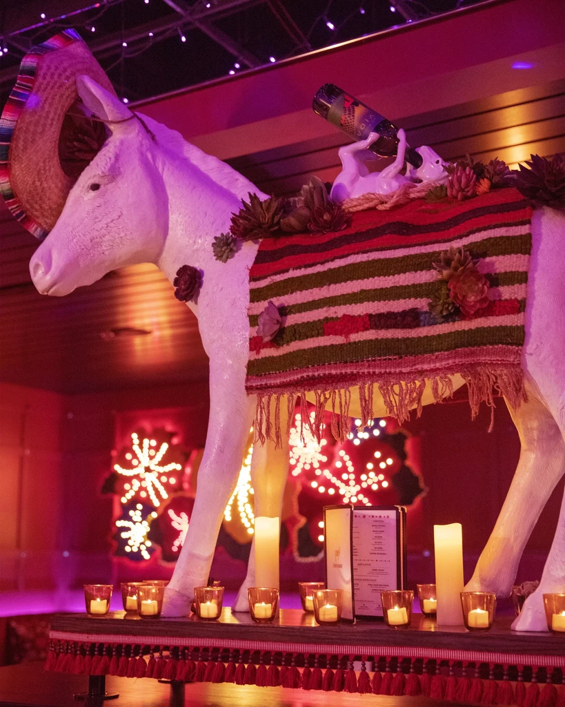 White donkey statue with sombrero and blanket in a vibrant, candlelit restaurant.