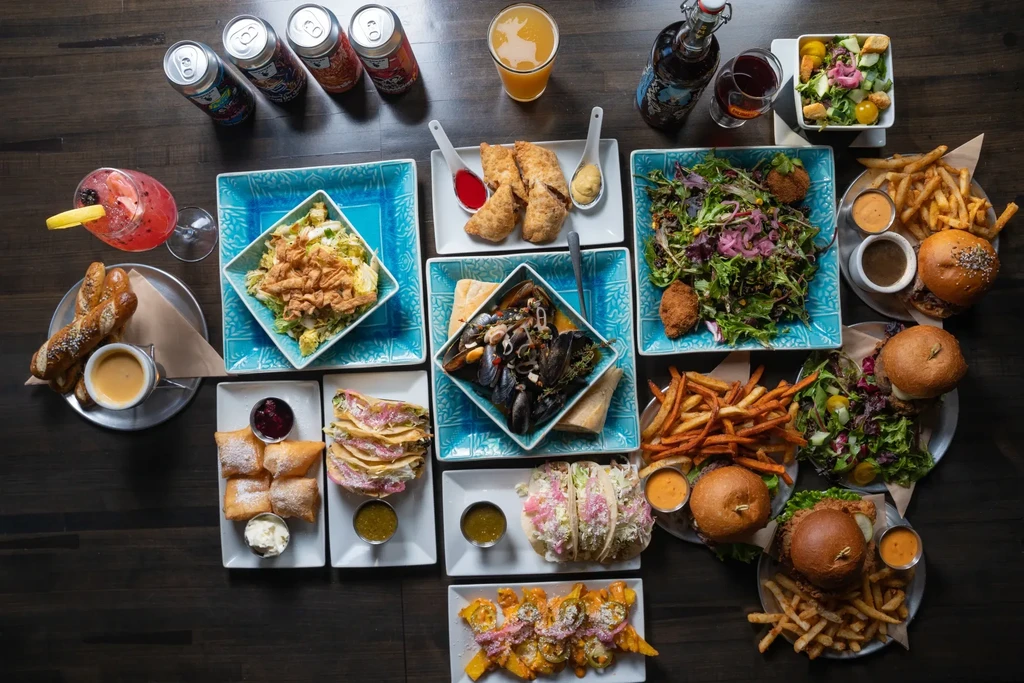 Overhead flat lay of diverse foods: salads, burgers, tacos, and drinks.