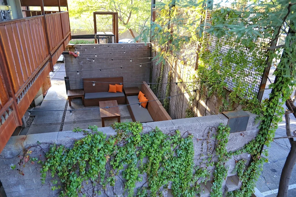 Sunken concrete patio with string lights, wooden benches, and vines.