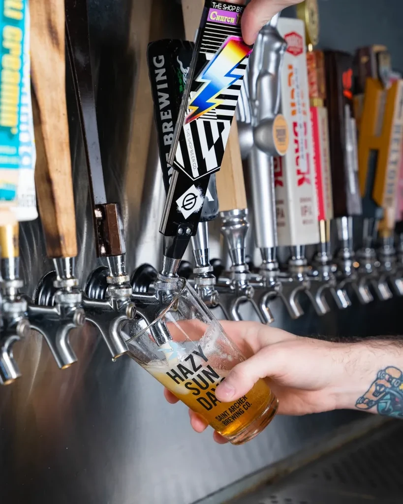 Hand pours pale amber beer from a tap into a branded glass.