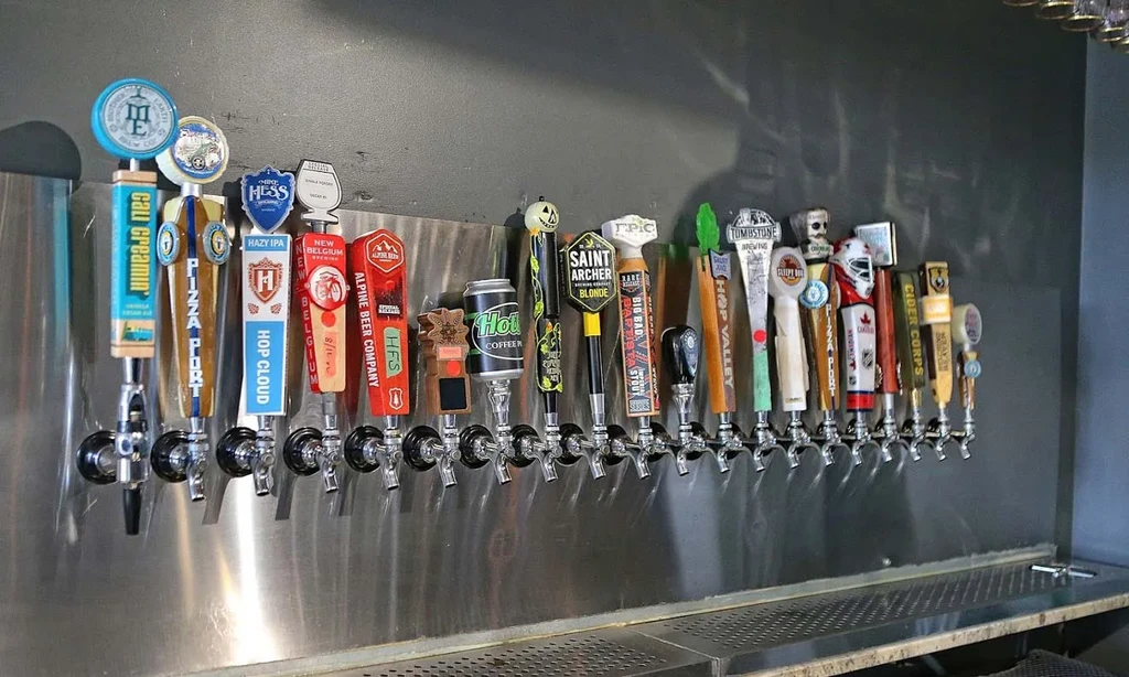 Twenty-five unique beer, cider, and coffee taps on a stainless steel wall.