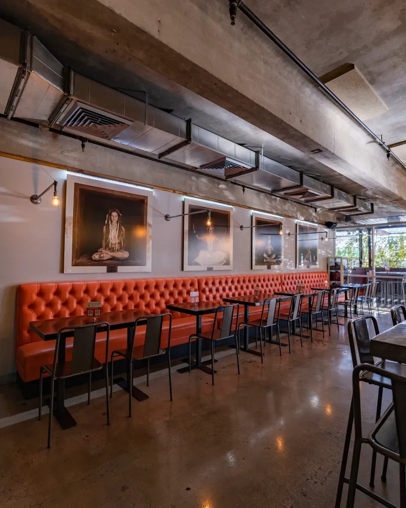 Empty industrial dining room with vibrant orange booth and artworks.