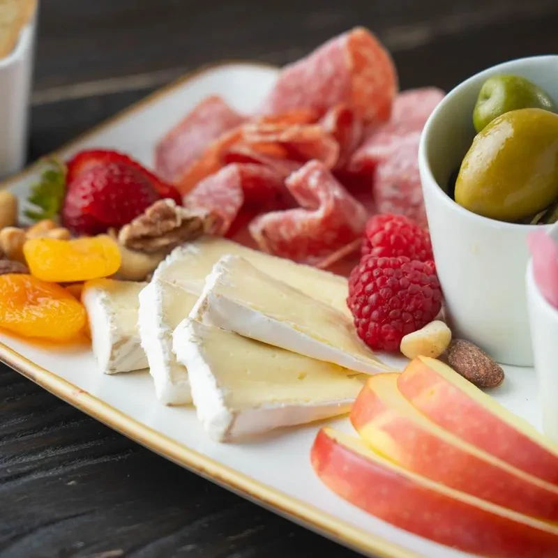 Close-up of a charcuterie board with brie, cured meats, fruit, and olives.