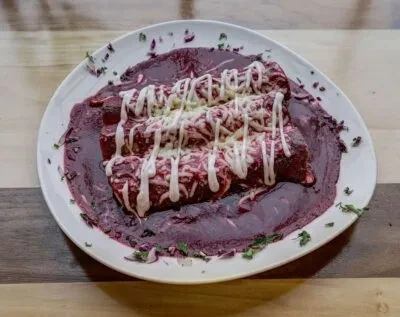 Three enchiladas with reddish-purple sauce, cheese, crema, and green herbs.