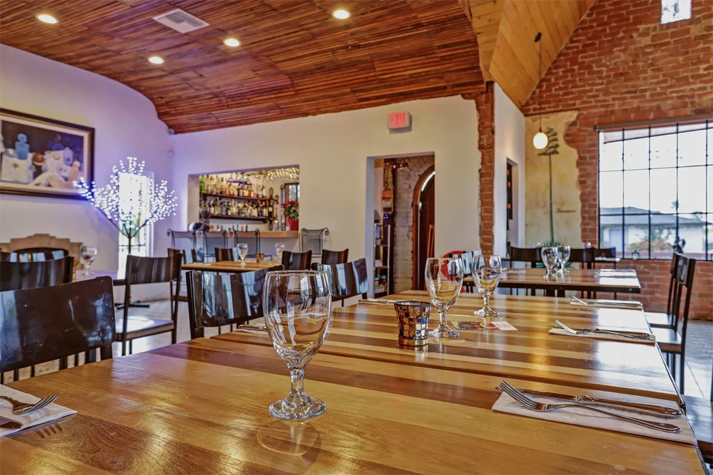 Empty rustic-modern restaurant interior with set tables and a visible bar.