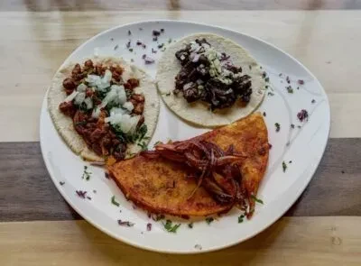 Overhead view of three distinct tacos on a white plate.