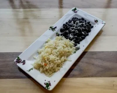 Rectangular white plate with rice, black beans, cheese, green garnish.