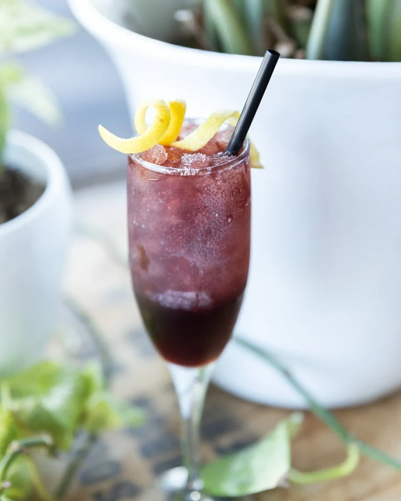 Layered frozen red drink in a stemmed glass with a lemon spiral.