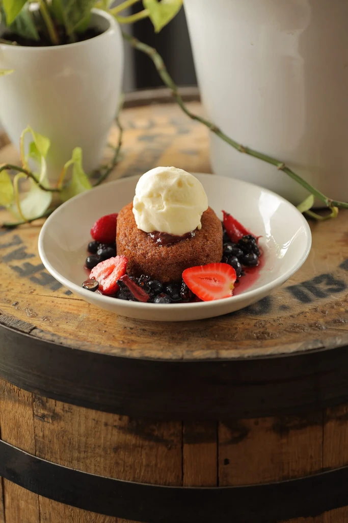Golden-brown cake with ice cream, red jam, and mixed berries.