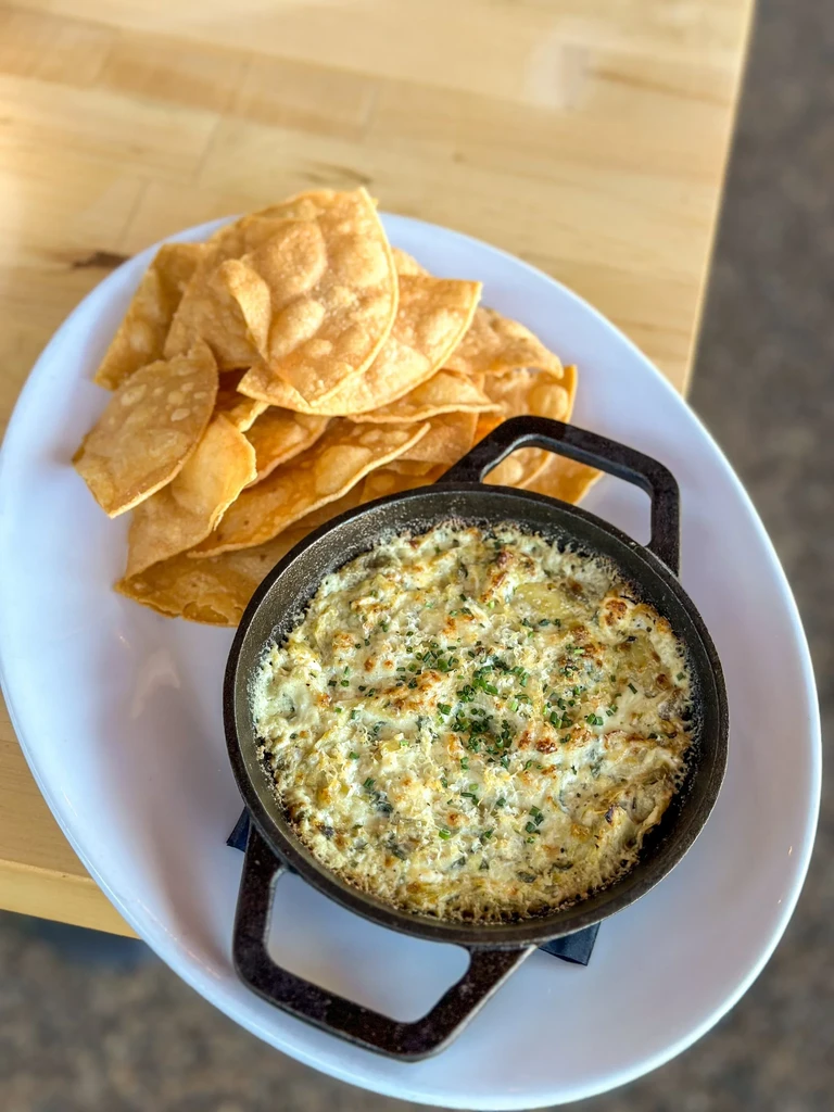 Hot dip in cast-iron skillet with green herbs and tortilla chips.