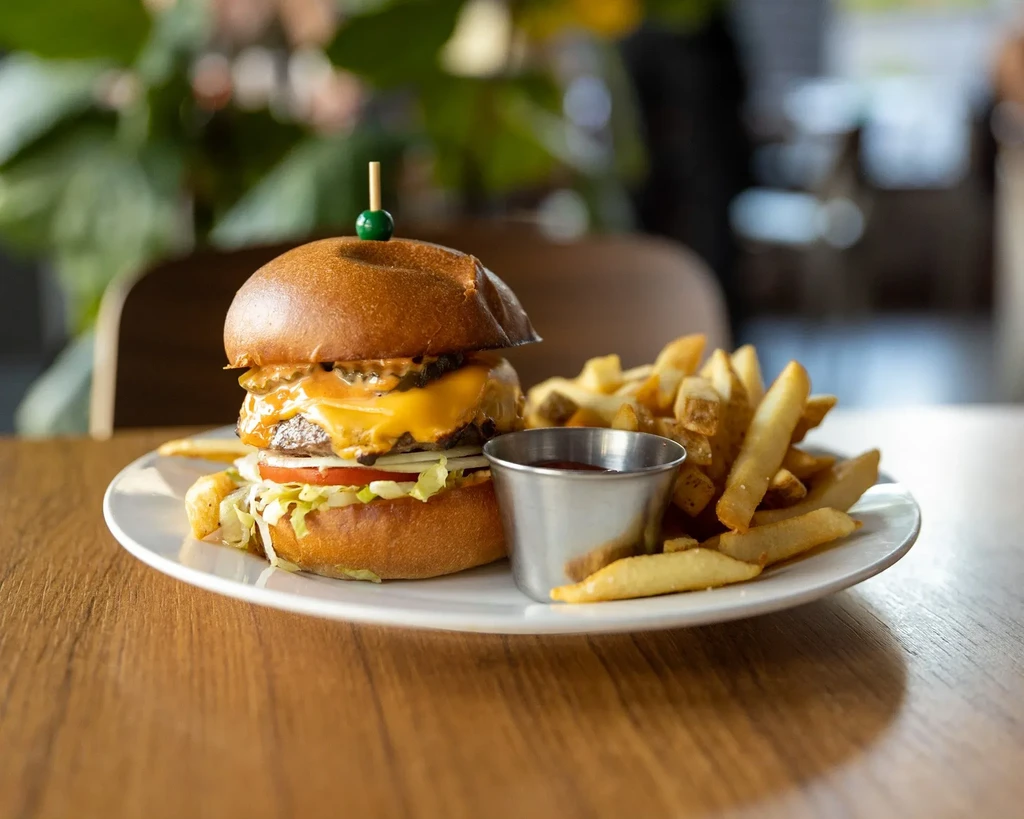 Burger with pickle spear, melted cheese, crispy fries, and sauce.