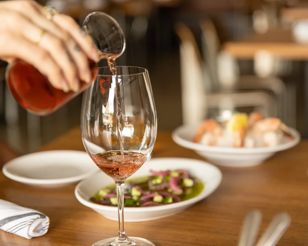 Hand pouring rosé wine into a glass at a restaurant table.