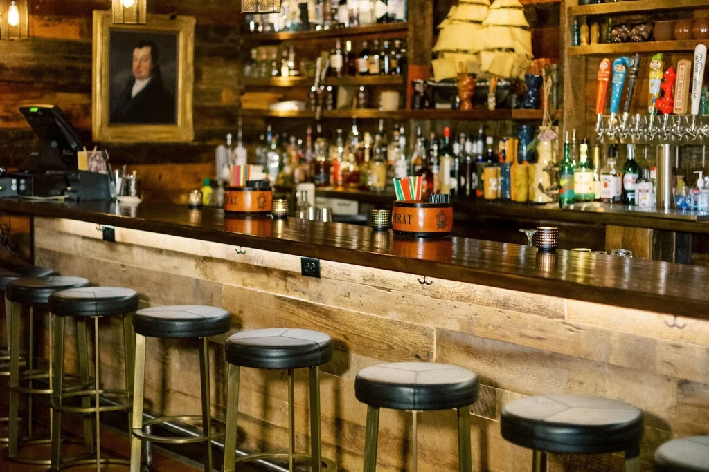 Empty wooden bar with stools, liquor bottles, and a ship model.