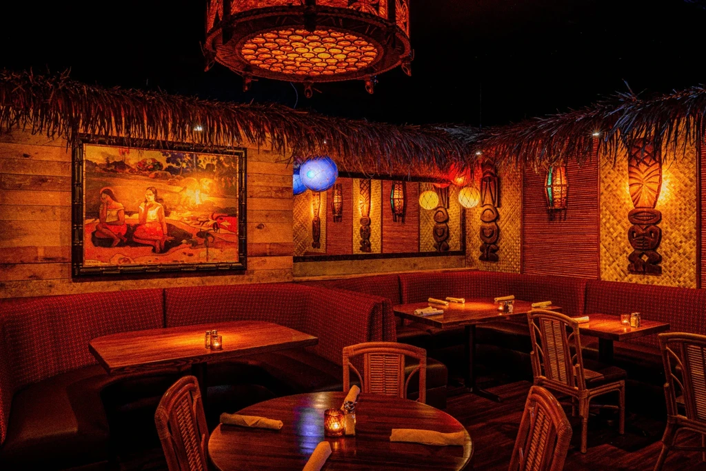 Tiki-themed restaurant interior with warm lighting, carved figures, and banquettes.