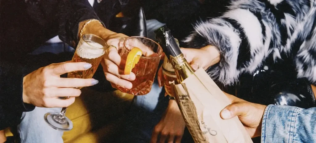 Close-up of hands holding a flute, cocktail, and champagne bottle.