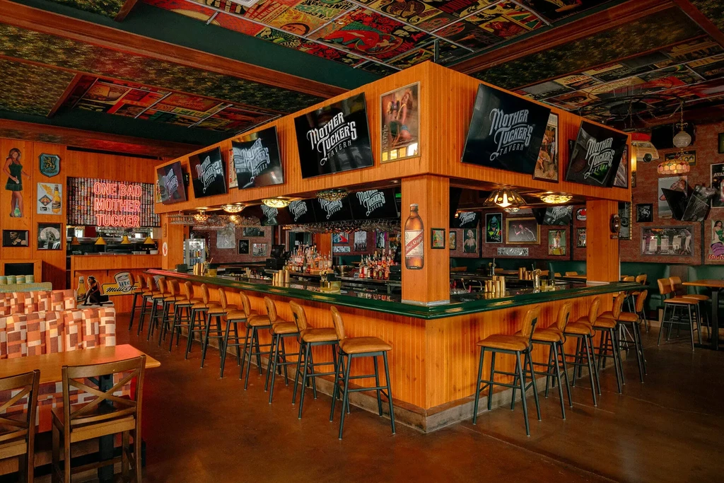 Retro tavern interior with a large bar, checkered booths, and vintage signs.