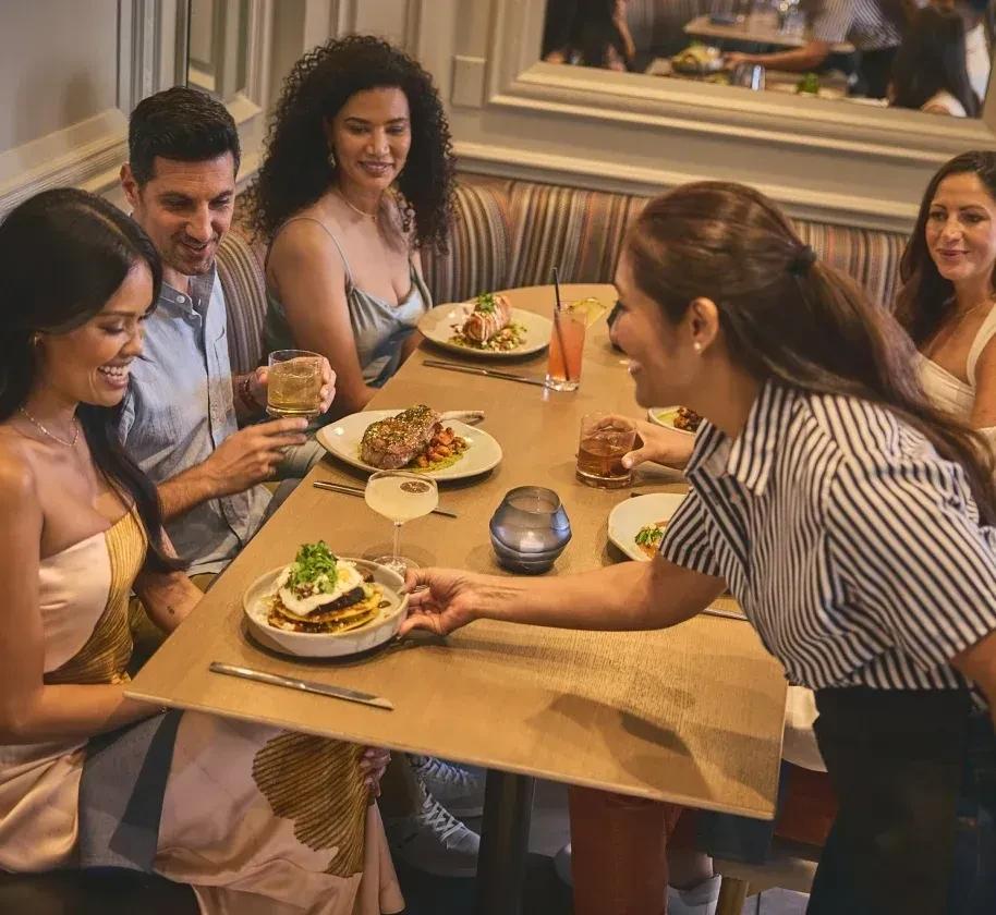 Server places food for five diners at a lively restaurant.