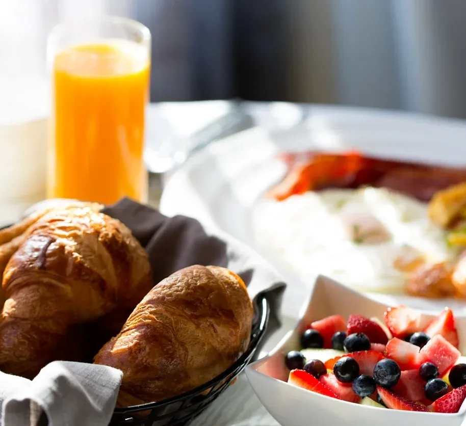 A bright breakfast spread with croissants, fruit salad, orange juice, and eggs.