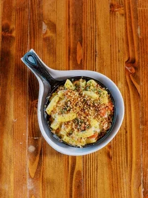 Creamy mac and cheese in skillet, breadcrumbs and herbs, on wood.