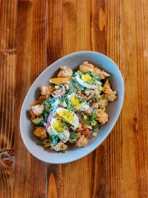 Crispy fried chicken salad with eggs on a rustic wooden table.