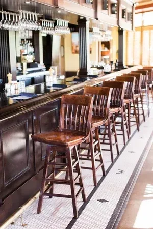 A long dark wooden bar, stools, hanging wine glasses, tiled floor.