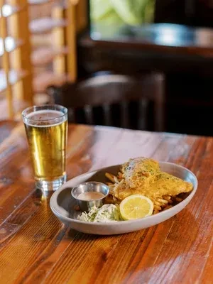 Crispy fish and chips, coleslaw, lemon, and cold beer on wood.