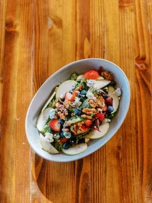 Colorful salad with greens, apple, berries, blue cheese, walnuts on wood.