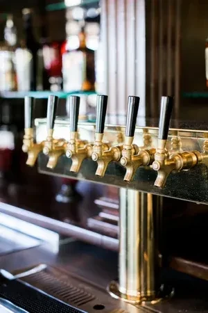 Polished brass beer taps with black handles on a bar counter.