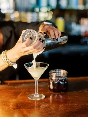 Hands pour cocktail from silver shaker into a martini glass.