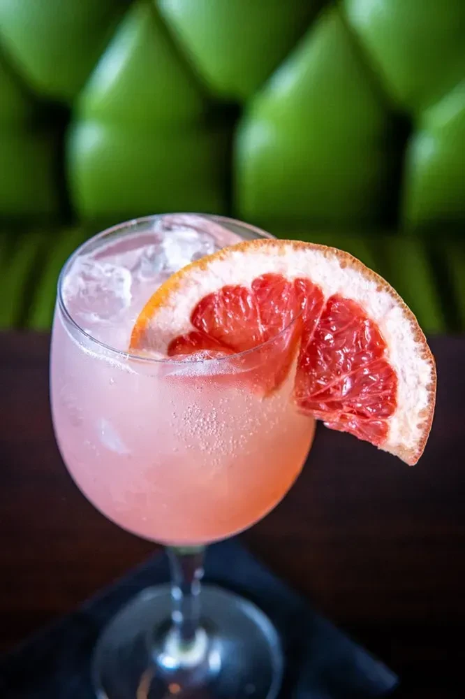 Sparkling pink cocktail with grapefruit garnish in stemmed glass.