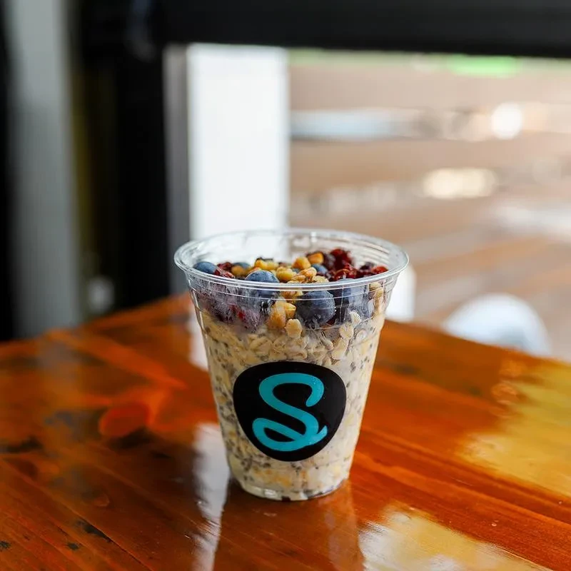 Layered parfait in clear cup with berries, nuts, and teal S logo.